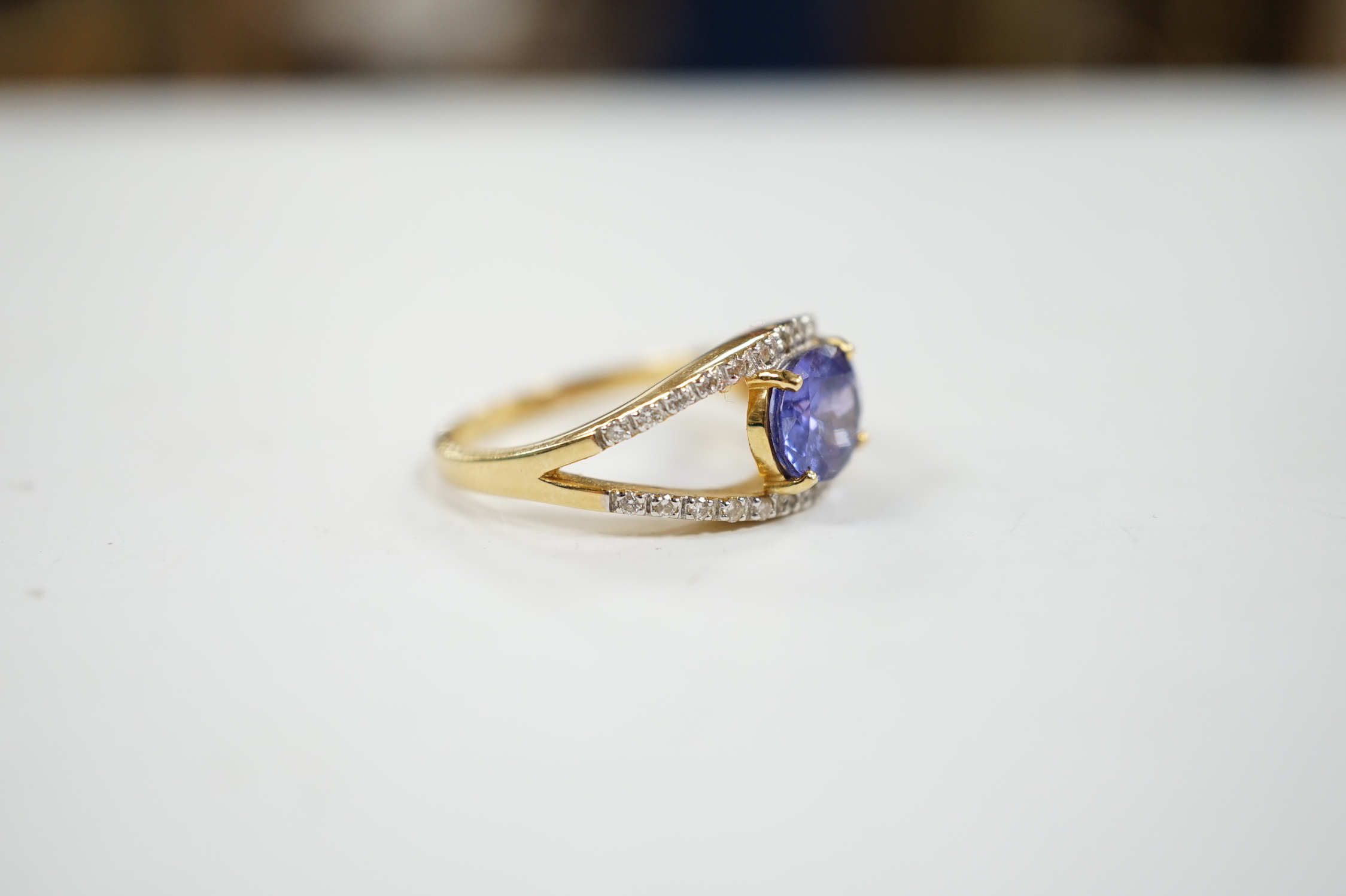 A modern 18ct gold and singe stone oval cut tanzanite ring, with diamond chip set borders, size N, gross weight 5 grams.